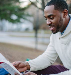 A man wearing a sweater reads an academic book.
