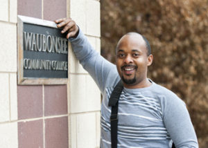 A middle-aged man leans against a community college building.