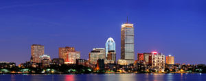 Boston city skyline at dusk with Prudential Tower and urban skyscrapers over Charles River with lights and reflections.